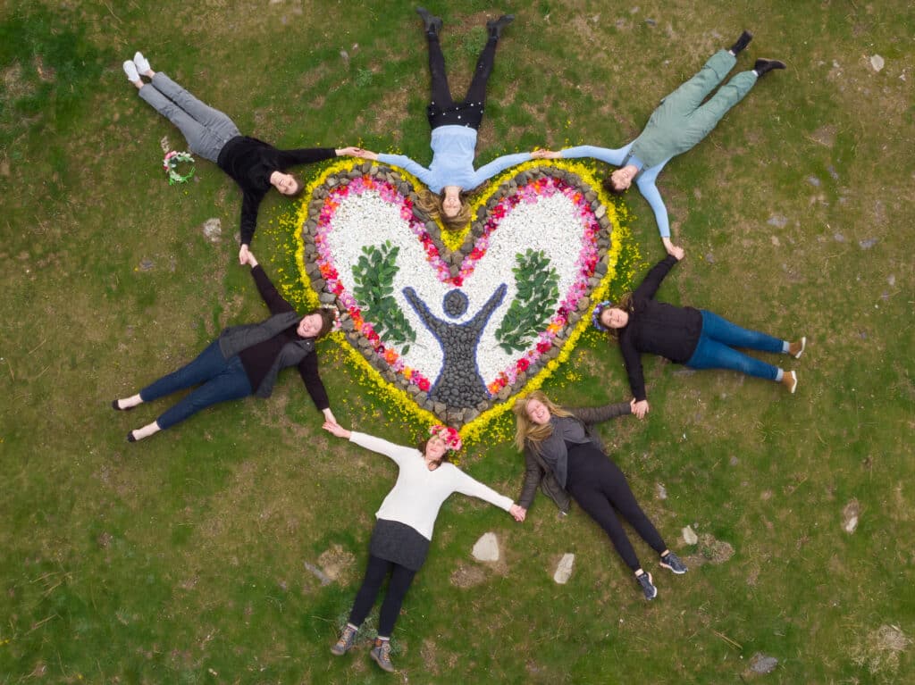 women encircle a floral artwork, holding hands.