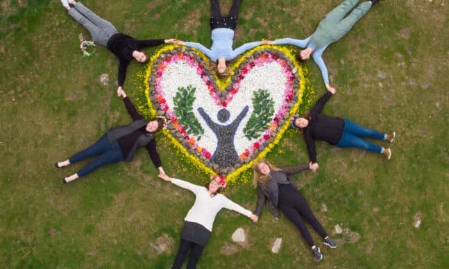 women encircle a floral artwork, holding hands.