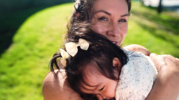Mother smiling holding her young child outside on a sunny day